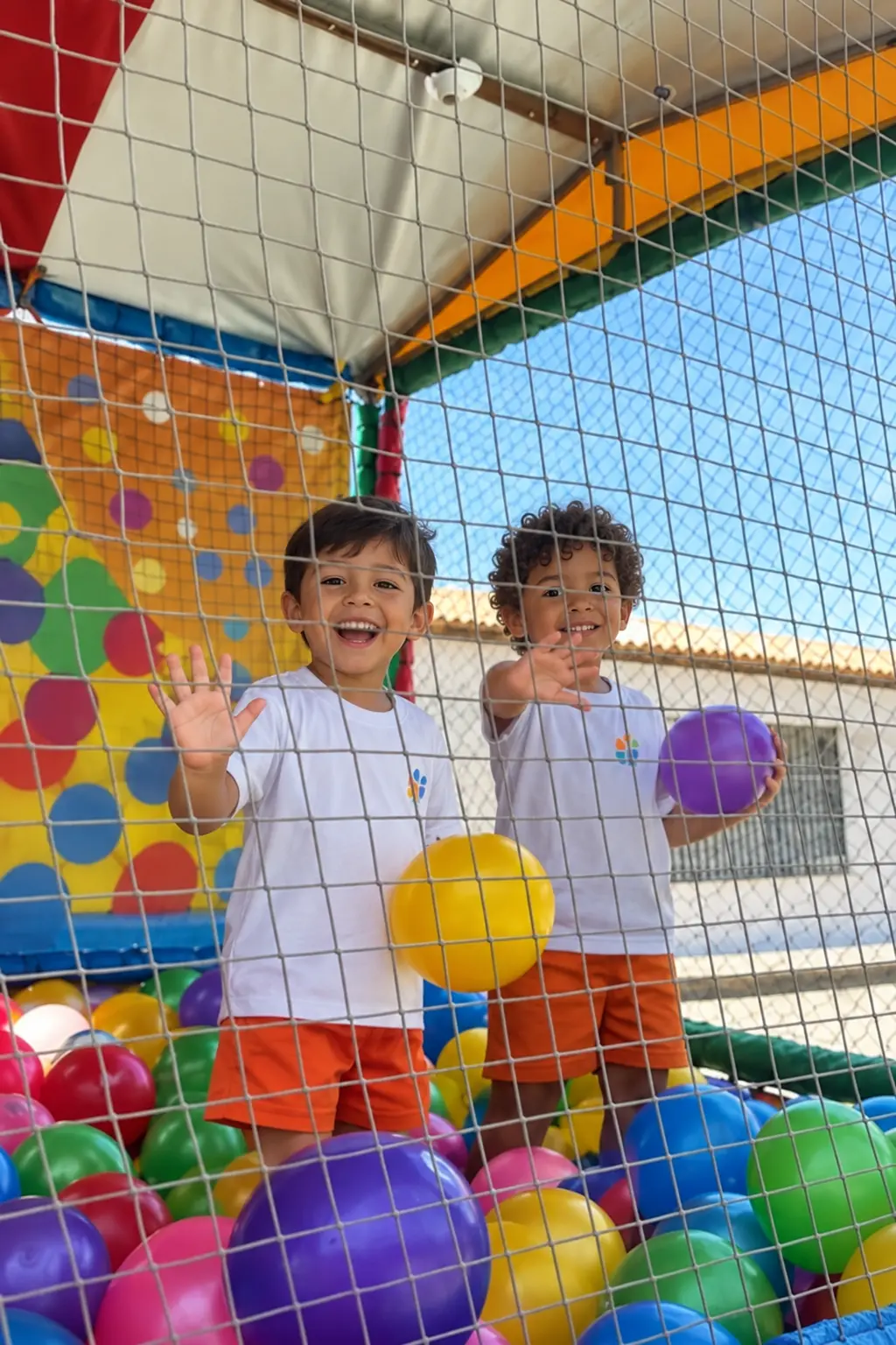 Dois alunos de farda acenando na piscina de bolinhas